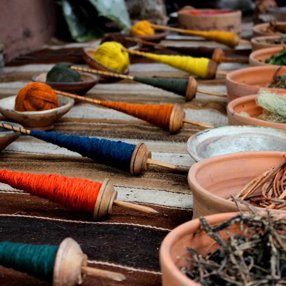 Madejas de hilo teñidas junto a cuencos con materia vegetal seca sobre una mesa de trabajo